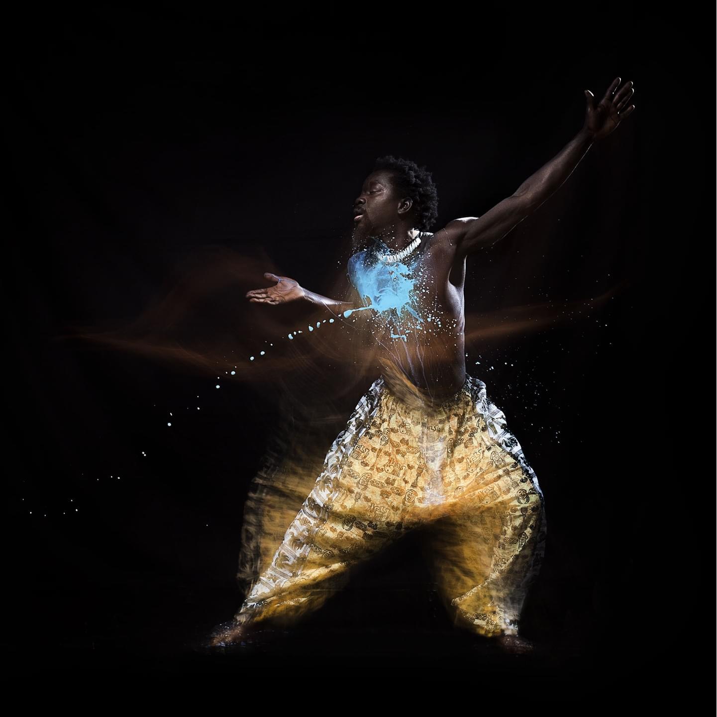 Senegalese dancer is being hit by blue water from the left.