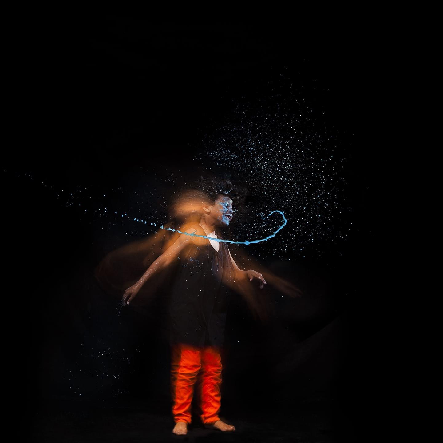 Long exposure photo of a child shaking his head after being hit by stylized blue water from the left.